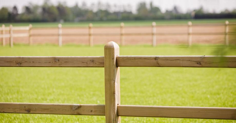 Una valla de madera con dos travesaños y postes cuadrados alrededor de un campo